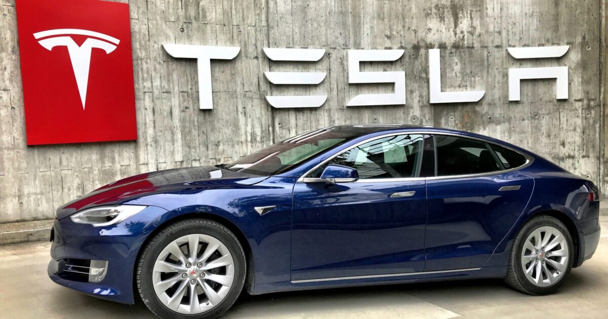 Tesla Model Y diante de um muro com a marca Tesla