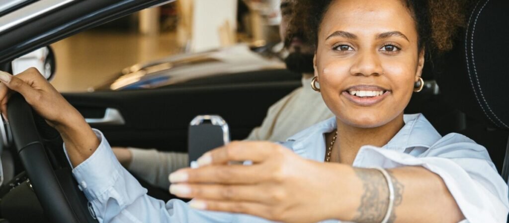 Imagem mostrando mulher num carro dentro de uma concessionária, segurando a chave na mão, sorrindo, indicando que comprou o carro