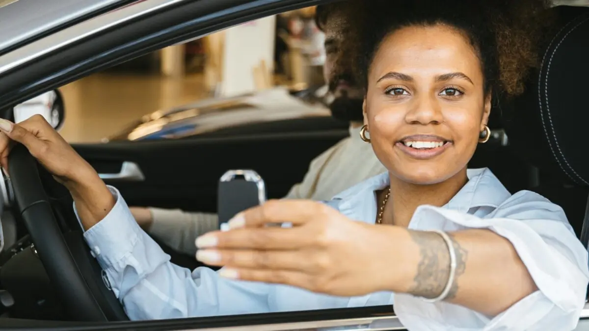 Imagem mostrando mulher num carro dentro de uma concessionária, segurando a chave na mão, sorrindo, indicando que comprou o carro