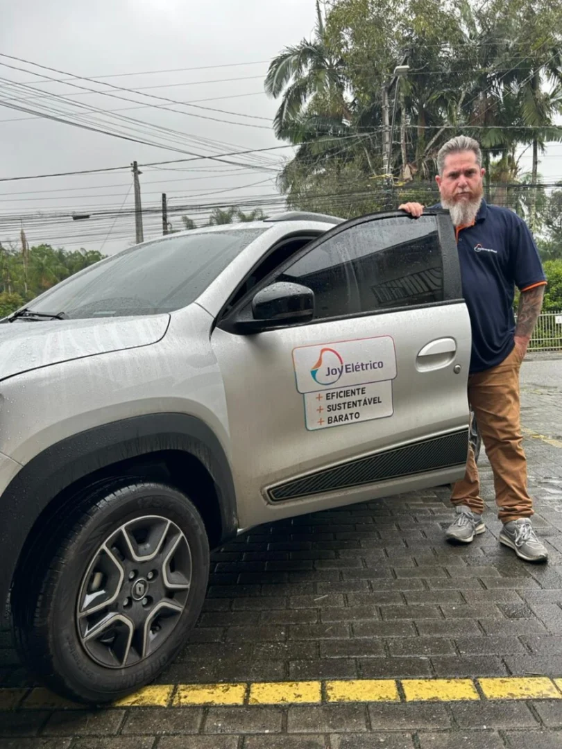 Foto de João costa, motorista de aplicativo que trocou para veículos elétricos, ao lado de seu carro alugado 