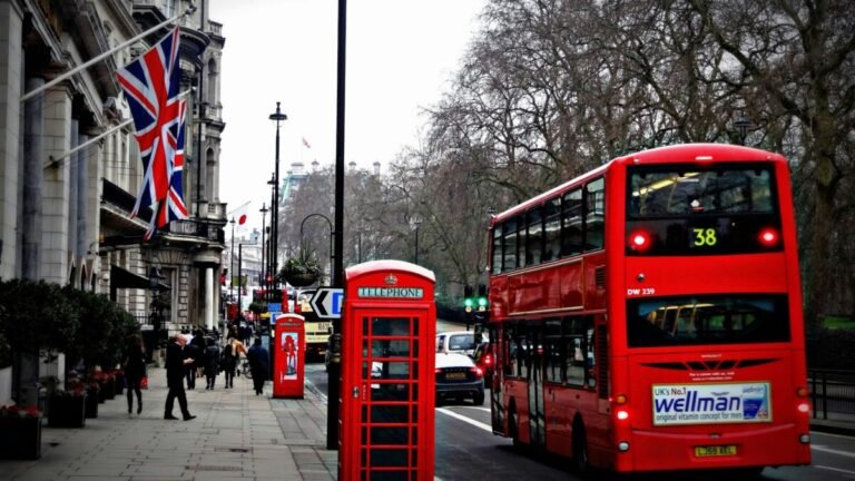 Foto de rua em Londres, com cabine, bandeiras e um ônibus de dois andares