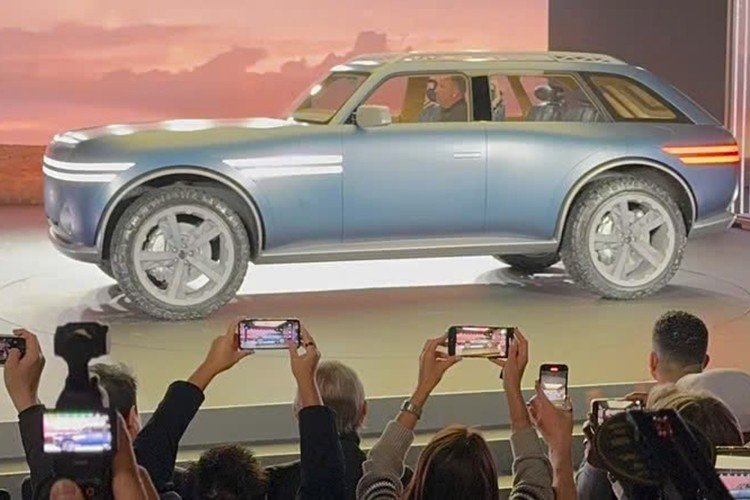 Genesis SUV off-road lateral. Veículo de grande porte de tintura escura, foco nas rodas dianteiras e traseiras. O público presente tira fotos