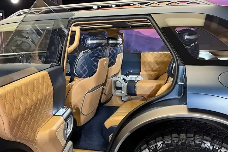 Imagem do carro Genesis SUV off-road, visão interna lateral. É possível ver todos os cinco bancos do veículo com detalhe para as cores (caramelo e azul marinho) e estampa (xadrez)