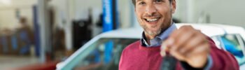 Foto de um homem segurando a chave de um carro, em frente a um carro, numa concessionária