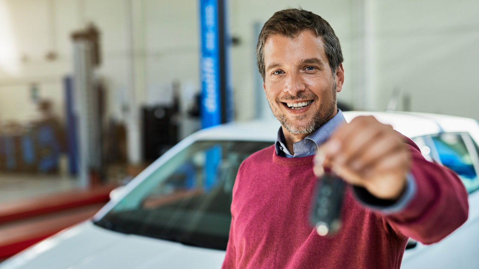 Foto de um homem segurando a chave de um carro, em frente a um carro, numa concessionária