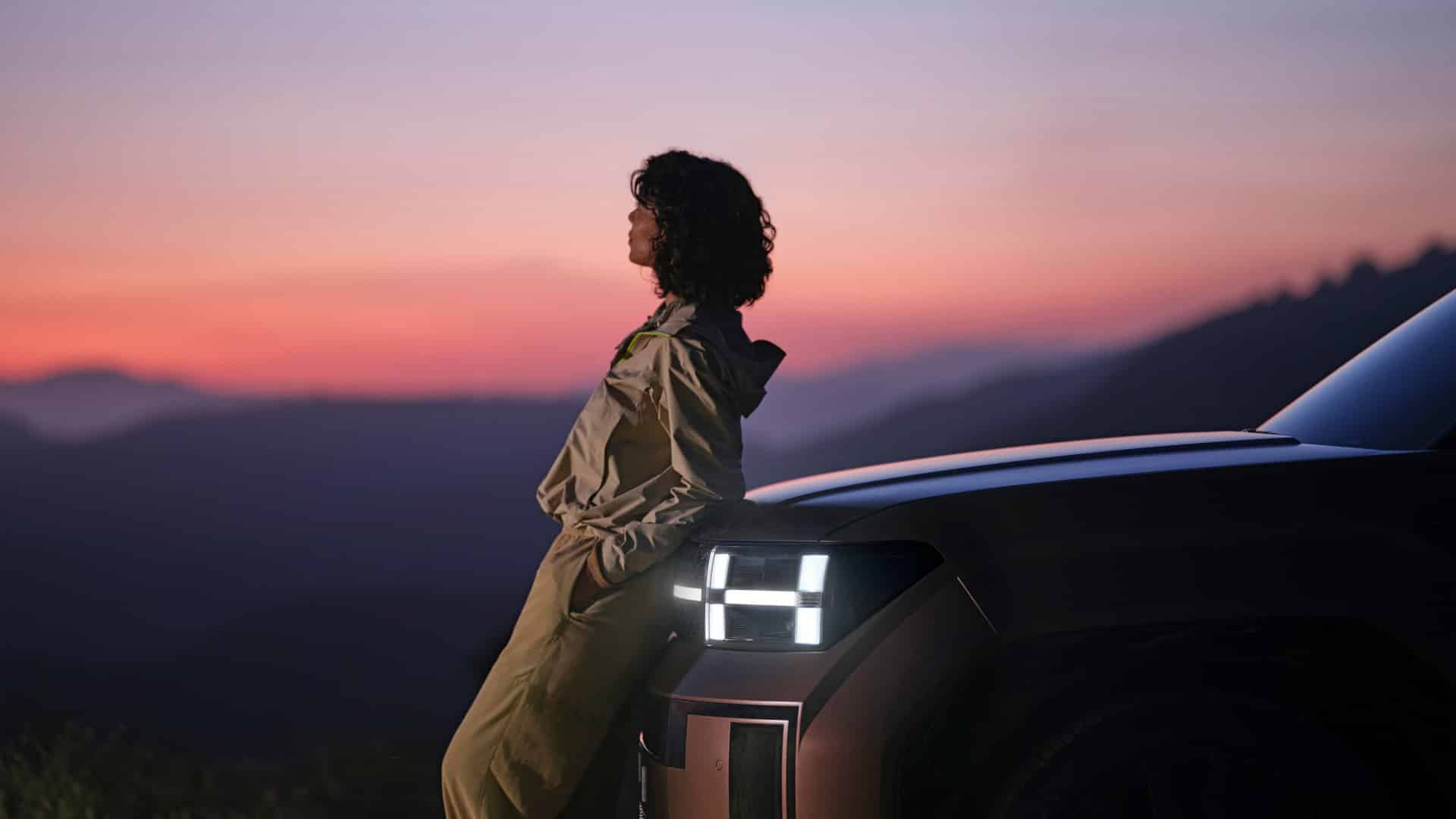 Mulher jovem encostada na frente de um Hyundai Ioniq 9, olhando o céu distante