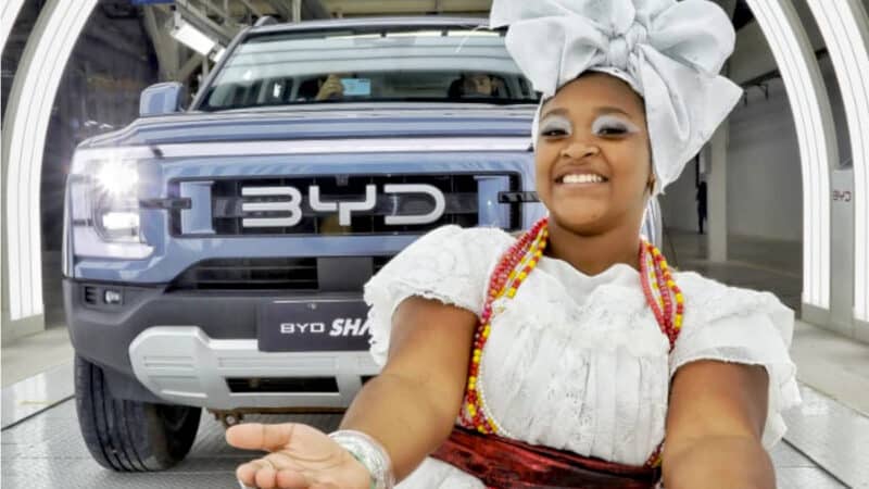 Modelo vestida de baiana na fábrica da BYD em Camaçari, com caminhonete BYD Shark ao fundo