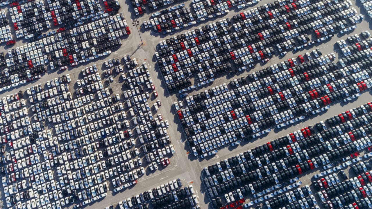 Milhares de carros aguardando transporte num porto, em foto aérea