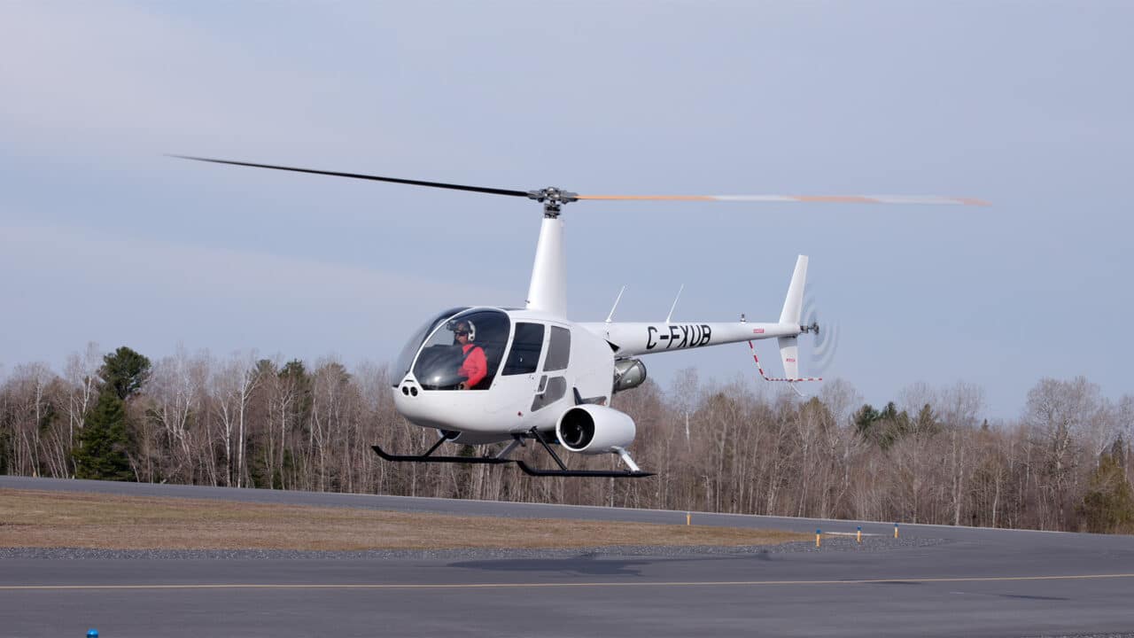 Helicóptero Robinson R44 do Project Proticity pairando sobre a pista do aeroporto
