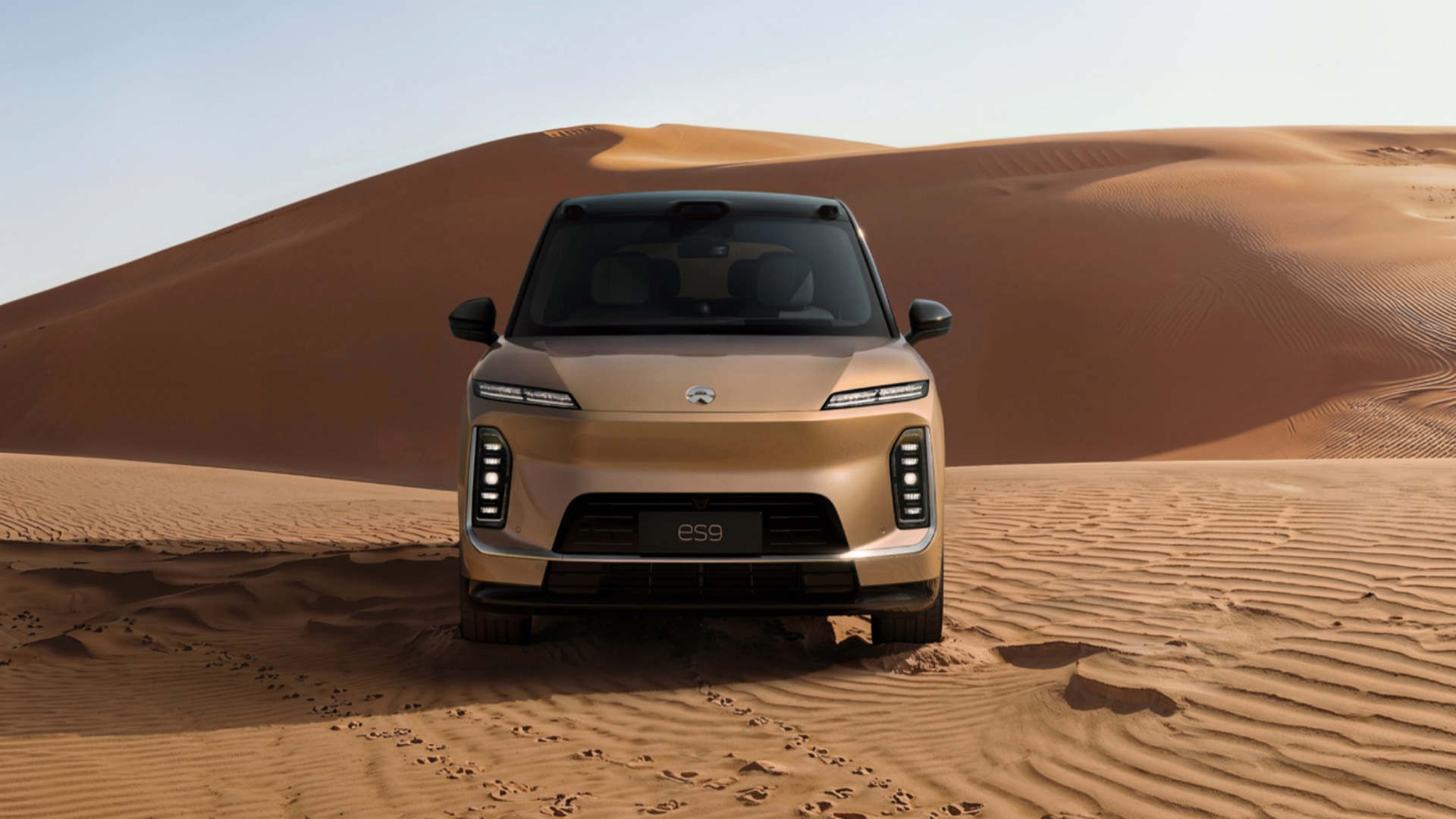 Detalhes da frente do SUV elétrico de luxo NIO ES9 em tom bege claro atravessando dunas no deserto
