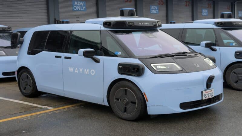 Robotáxi Ojai da Waymo, desenvolvido em parceria com a chinesa Zeekr, estacionado ao lado de outras unidades da frota. O veículo elétrico azul-claro conta com sensores, câmeras e sistema lidar no teto para operação autônoma nos Estados Unidos