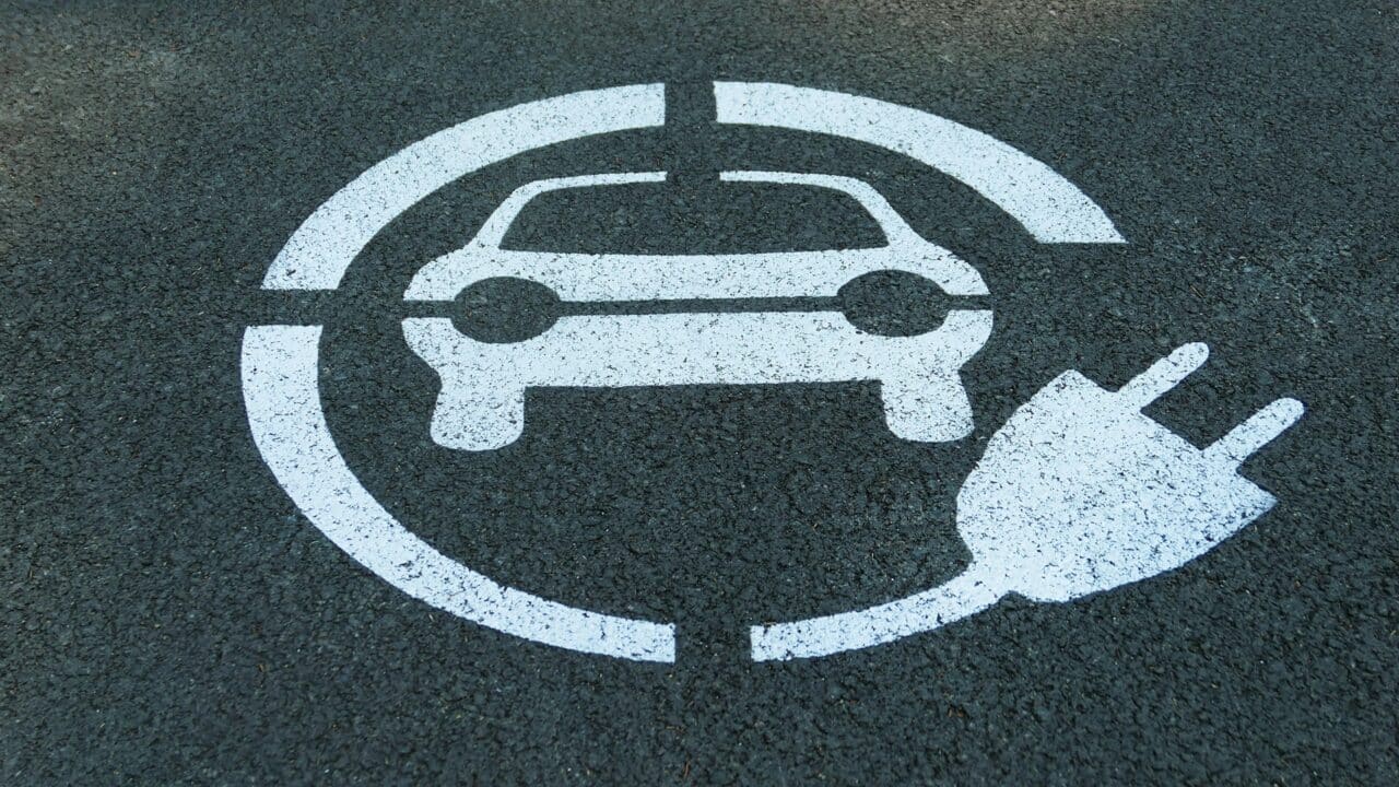 A imagem mostra a sinalização de uma vaga de recarga para veículos elétricos pintada diretamente no asfalto, em tinta branca