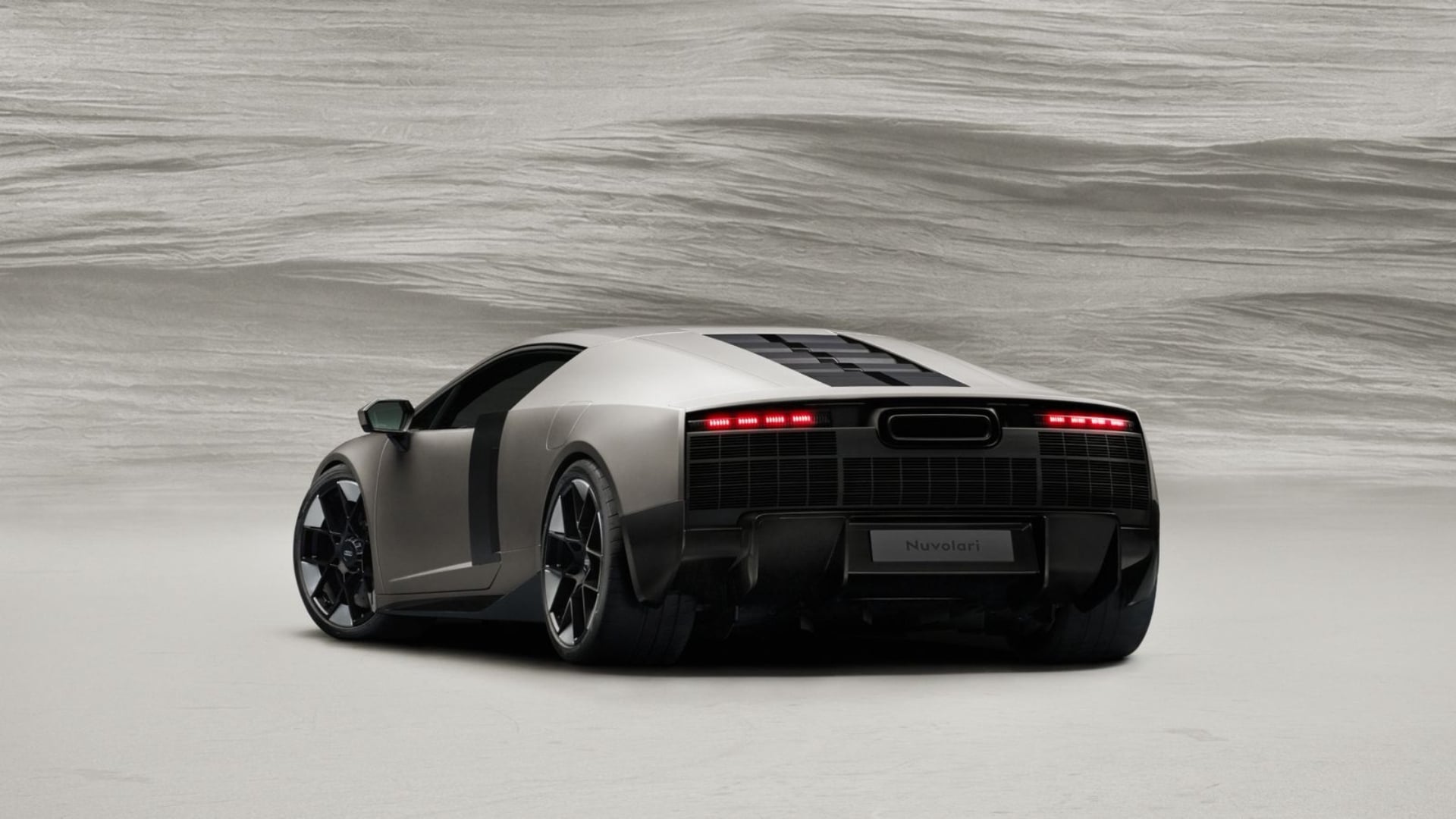 Vista traseira do Audi Nuvolari Concept em tom chumbo, com lanternas traseiras em LED vermelho acesas, painel traseiro em preto fosco com textura quadriculada, placa "Nuvolari" e rodas esportivas pretas