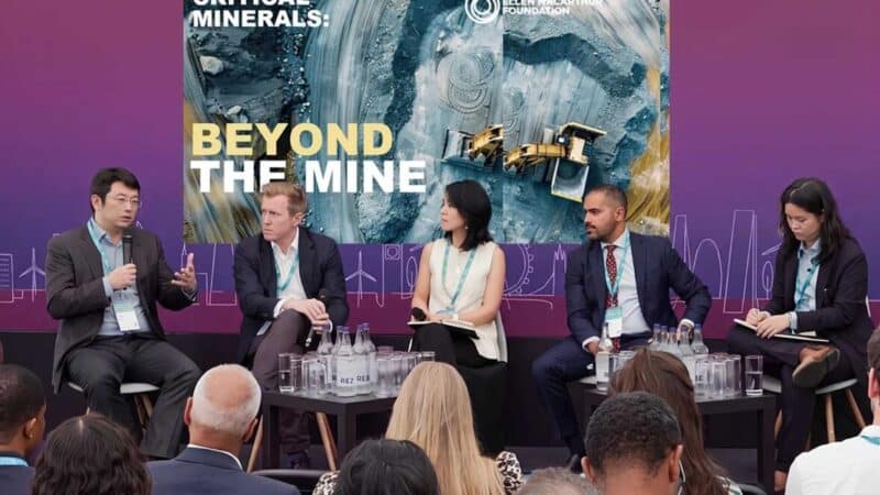 Fotografia de um painel de discussão com cinco palestrantes formais sentados em um palco