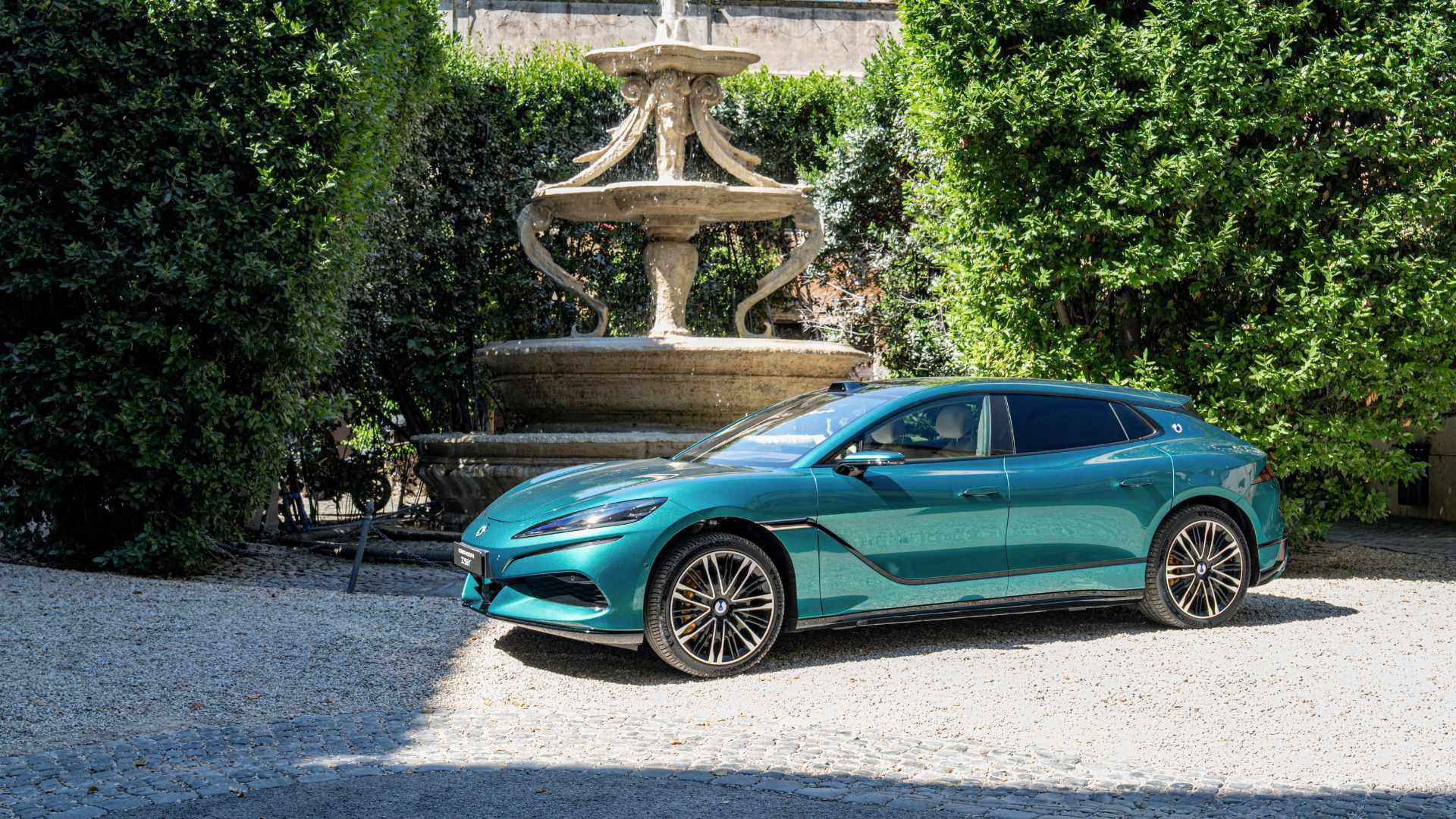Denza Z9GT verde estacionado em jardim histórico, com fonte de pedra ao fundo
