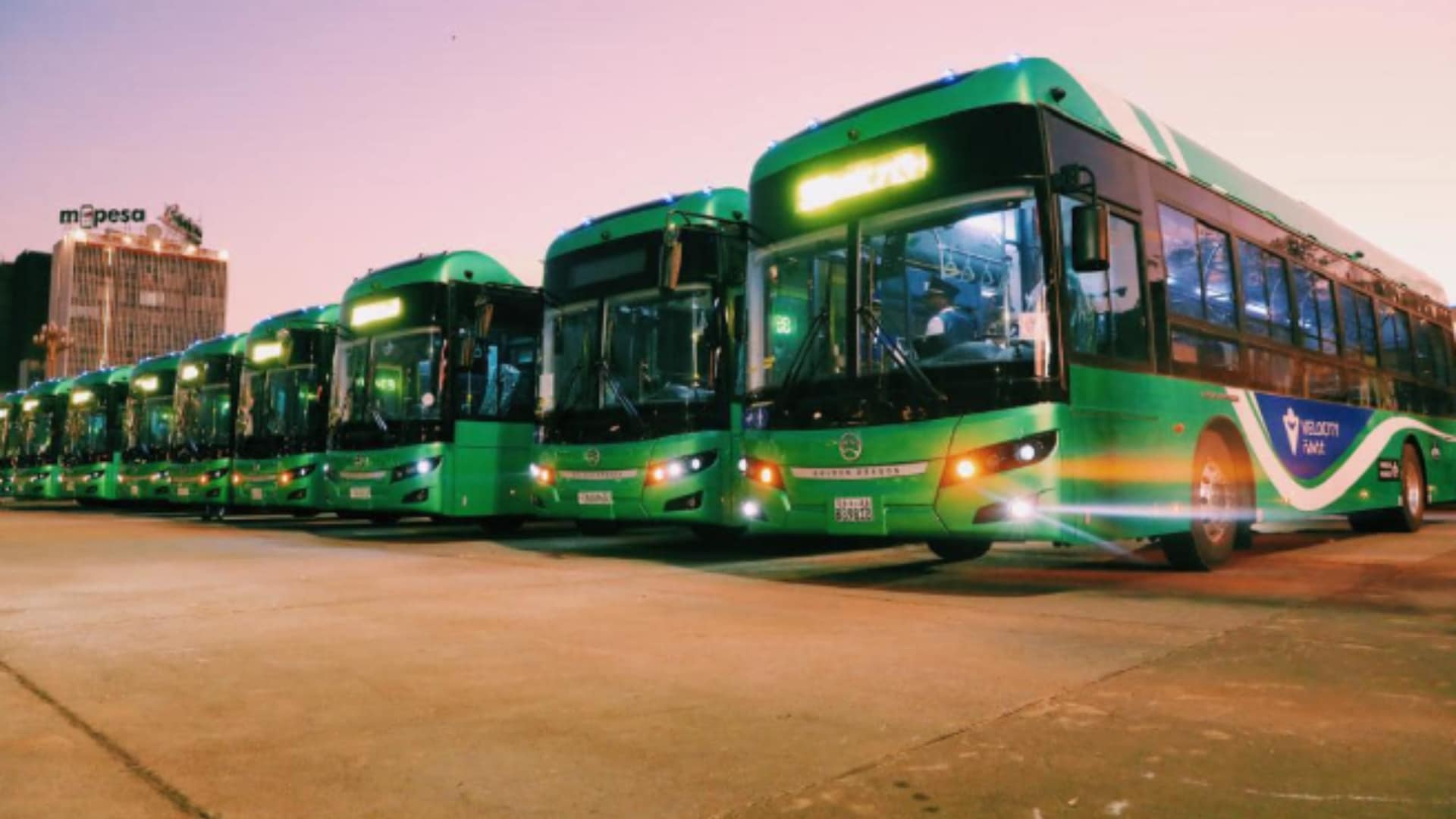 Fila de ônibus elétricos verdes estacionados em área urbana durante o entardecer, destacando a expansão do transporte sustentável na África
