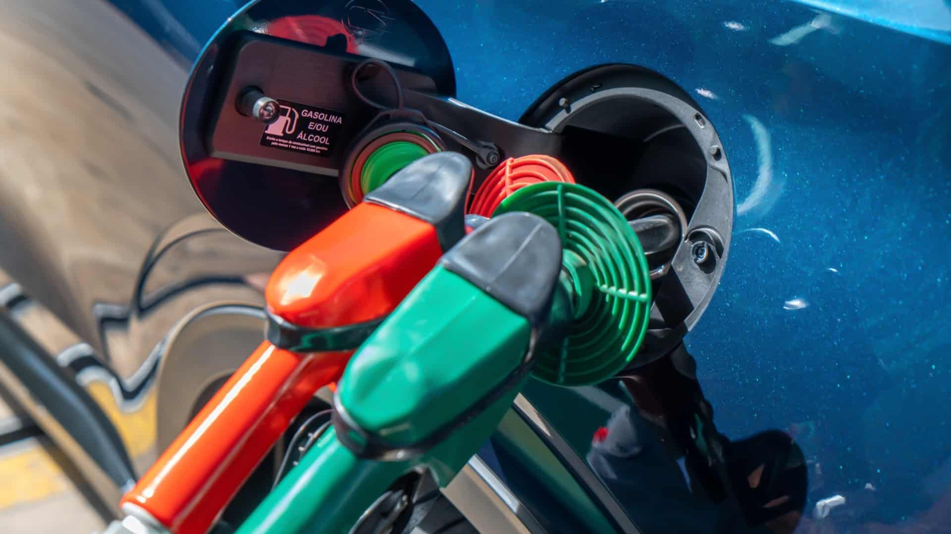 Bicos de combustível abastecem um SUV híbrido flex, com opções de gasolina e etanol destacadas na tampa do tanque