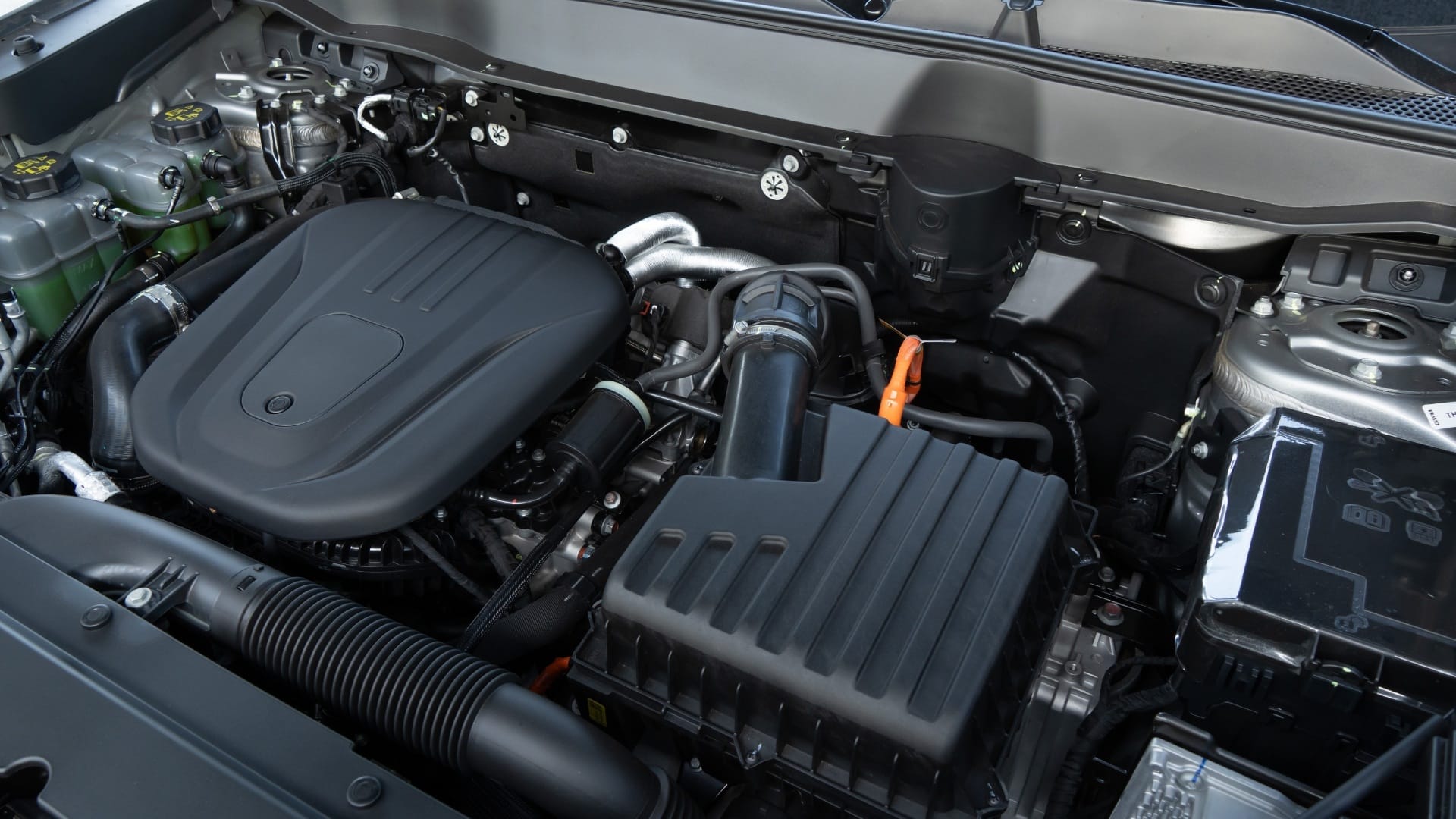 Compartimento do motor do GWM Haval H6 híbrido flex 2027, com conjunto híbrido à mostra, incluindo motor a combustão com tampa preta, cabos de alta tensão com conectores laranjas e reservatórios de fluidos