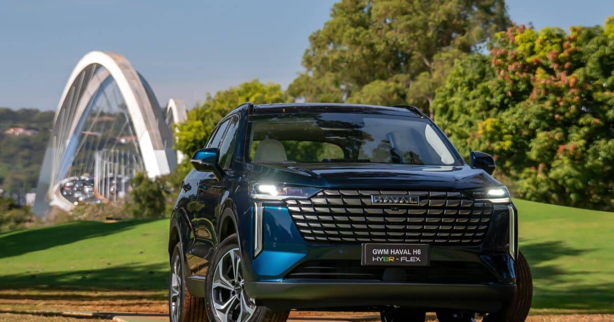 SUV GWM Haval H6 híbrido flex azul escuro estacionado em área verde, com ponte em arco ao fundo e árvores ao redor