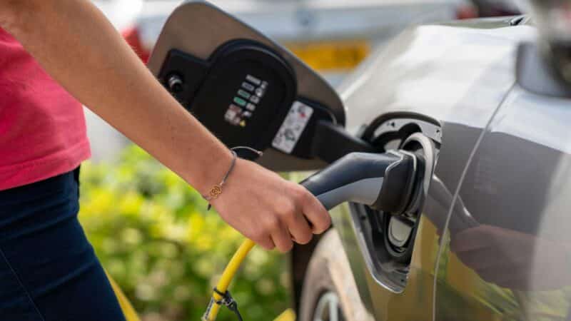 Pessoa conectando cabo de carregamento em carro elétrico em estação de recarga ao ar livre