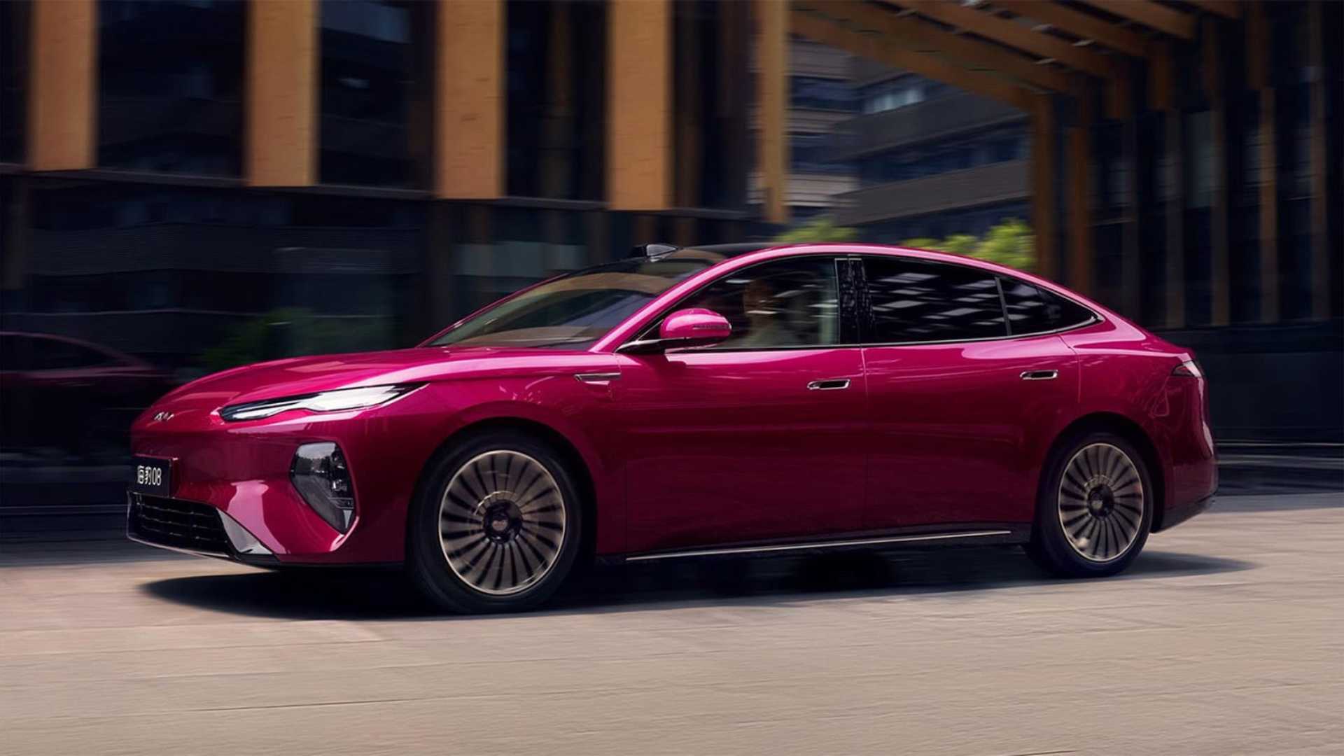 Sedã BYD Seal 08 na cor magenta ou rosa escuro, fotografado de perfil enquanto circula por uma rua urbana com prédios modernos ao fundo