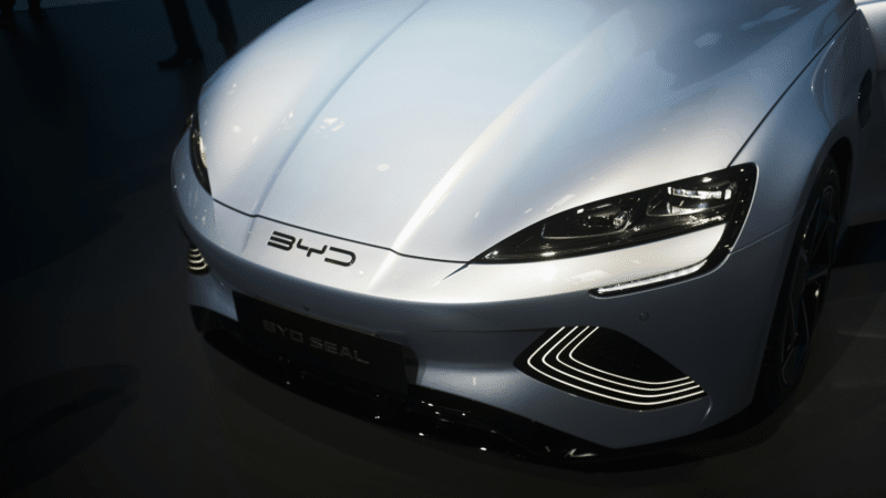 Detalhe da dianteira do carro elétrico branco BYD Seal, destacando seus faróis e logotipo em um showroom escuro