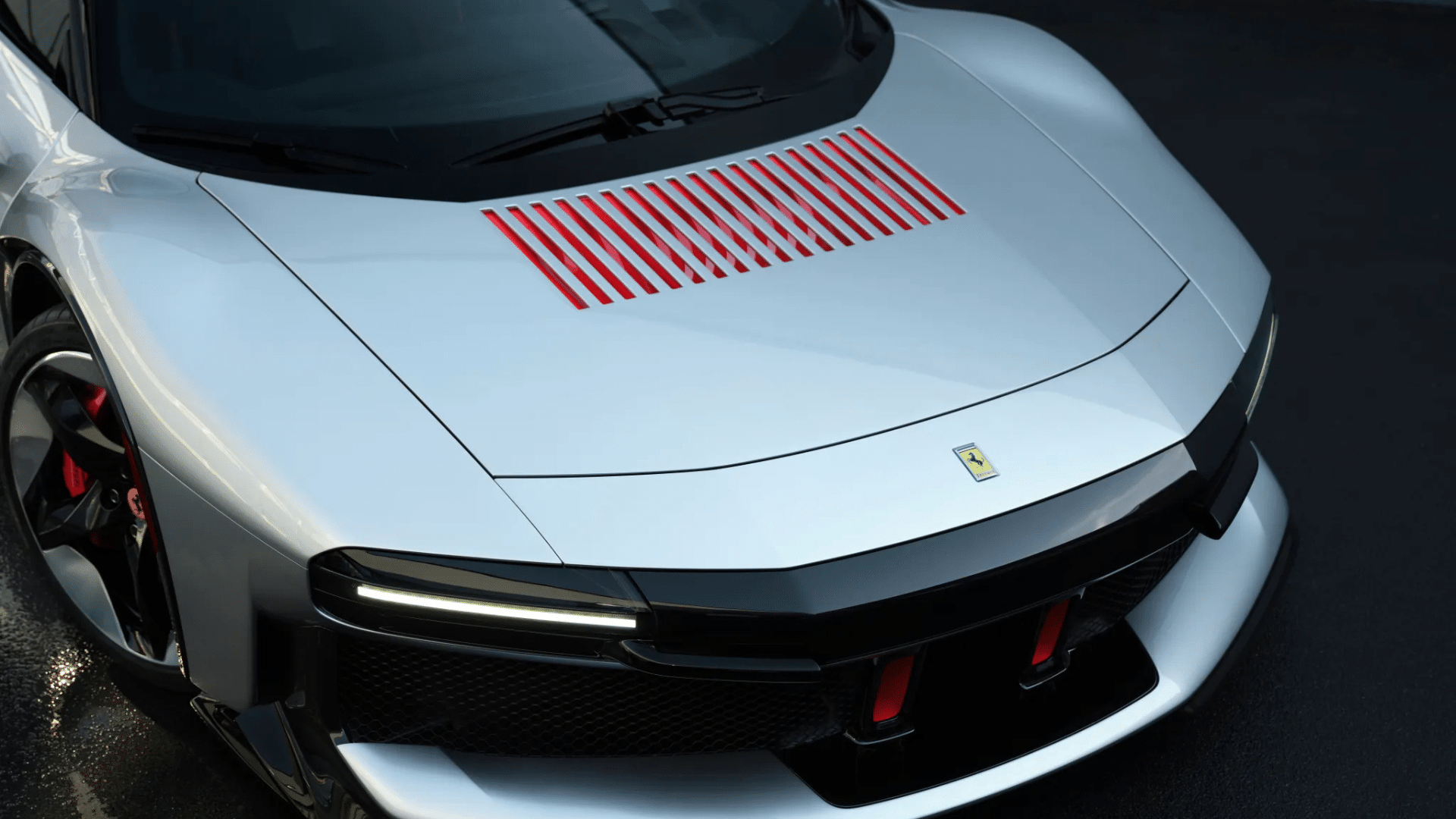 Detalhe frontal da Ferrari cinza com aberturas vermelhas no capô e faróis ultrafinos