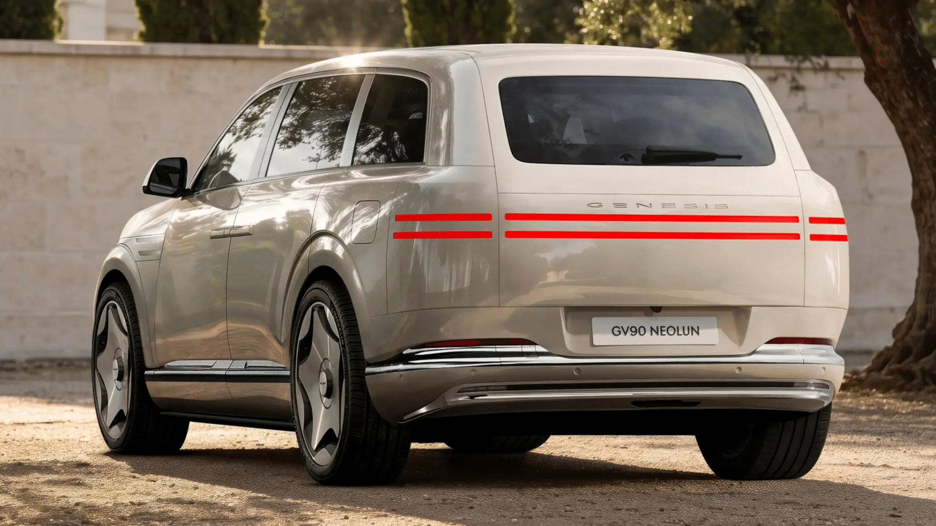 Traseira do SUV Genesis GV90 na cor prata metálica estacionado em área de terra. O design apresenta uma traseira limpa e elevada, com lanternas em LED em formato de duas linhas horizontais vermelhas atravessando a largura do veículo, para-choques com acabamento cromado e rodas aerodinâmicas de design fechado. Placa com a inscrição "GV90 NEOLUN"