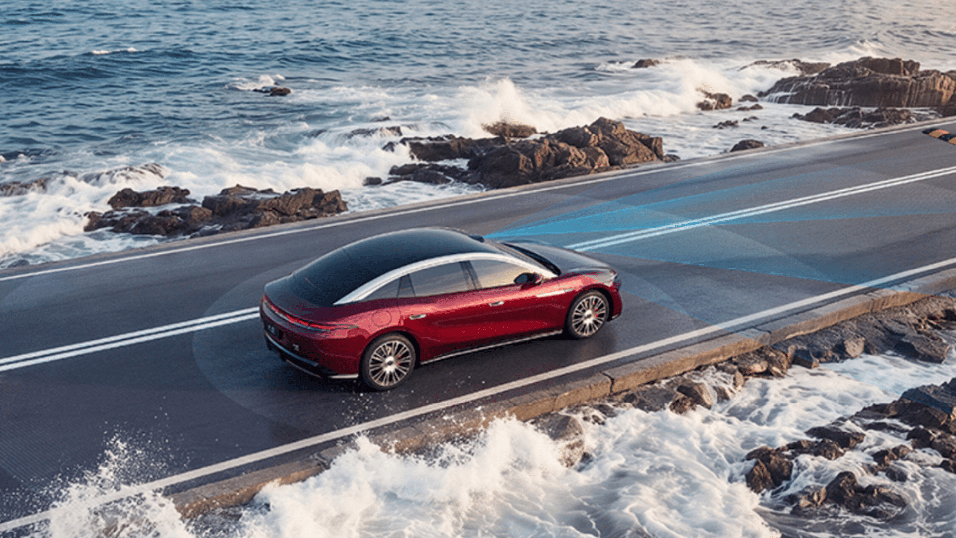 Vista aérea traseira de um Great Han vermelho-escuro dirigindo em uma estrada costeira ao lado do mar agitado, com ondas quebrando nas rochas e uma representação visual azul das ondas de radar do carro