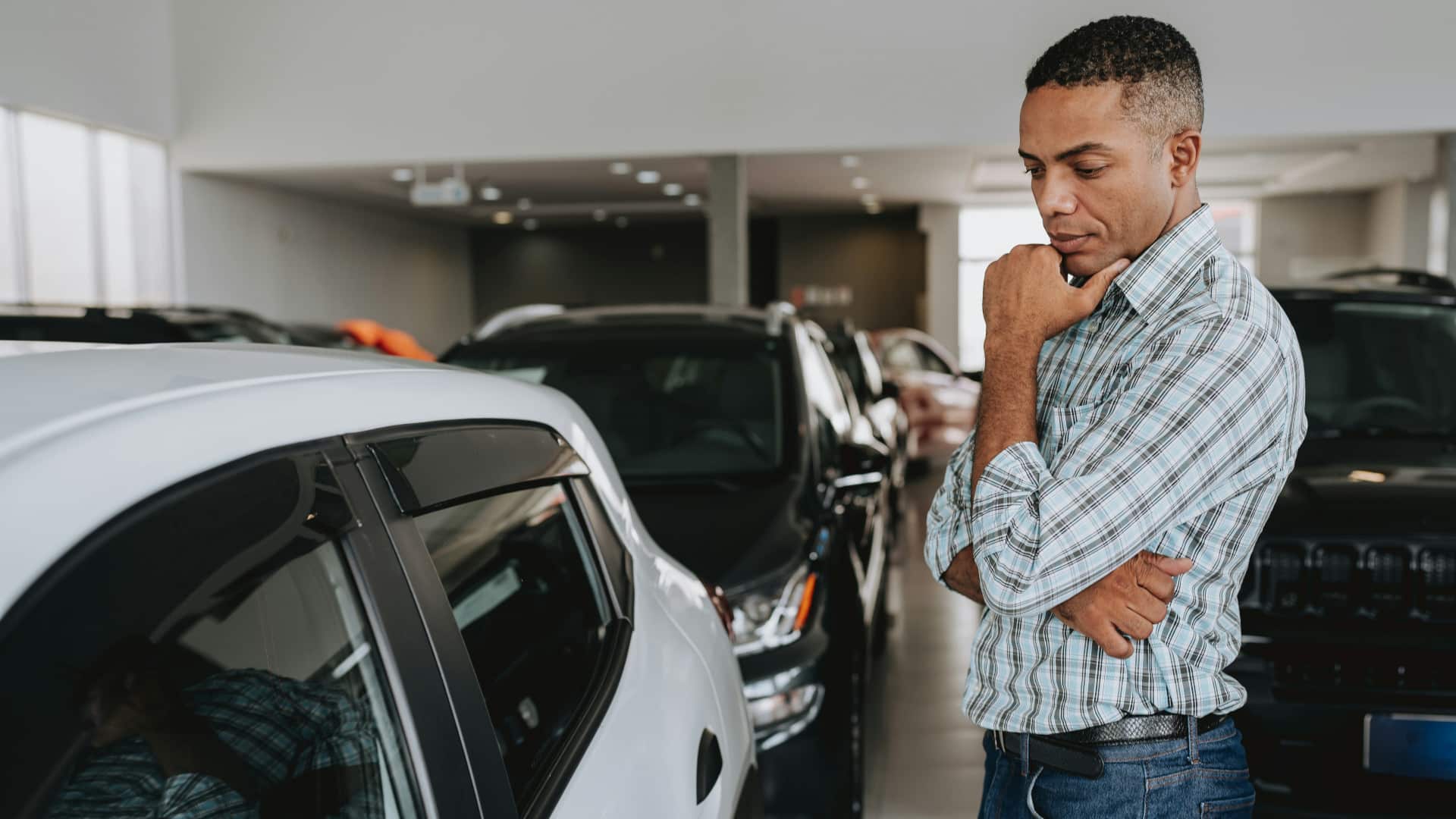 Foto de um homem olhando para um carro num pátio com muitos carros