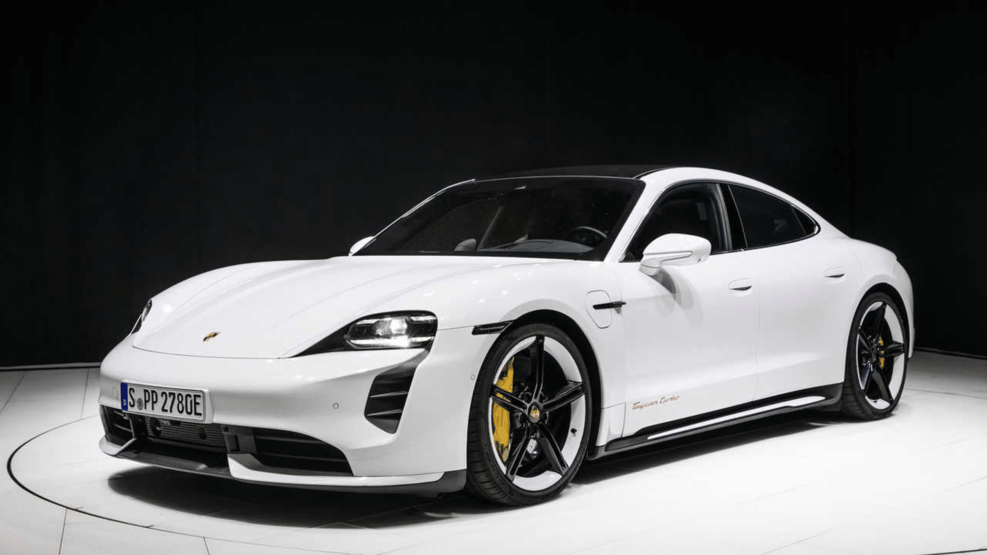 Porsche Taycan Turbo S branco em estúdio com fundo escuro, mostrando detalhes das rodas e a lateral do veículo