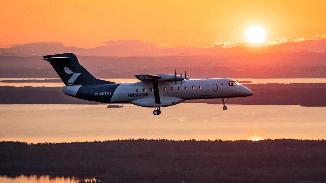 Avião elétrico Heart X1 voando com trem de pouso baixado contra um cenário de pôr do sol alaranjado sobre rio e montanhas