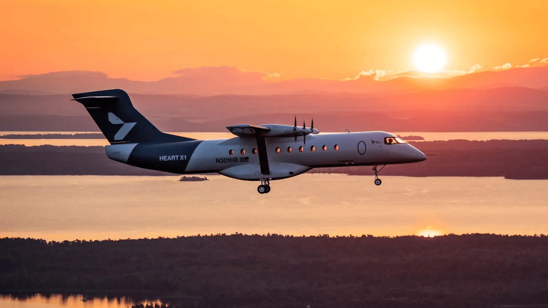 Avião elétrico Heart X1 voando com trem de pouso baixado contra um cenário de pôr do sol alaranjado sobre rio e montanhas