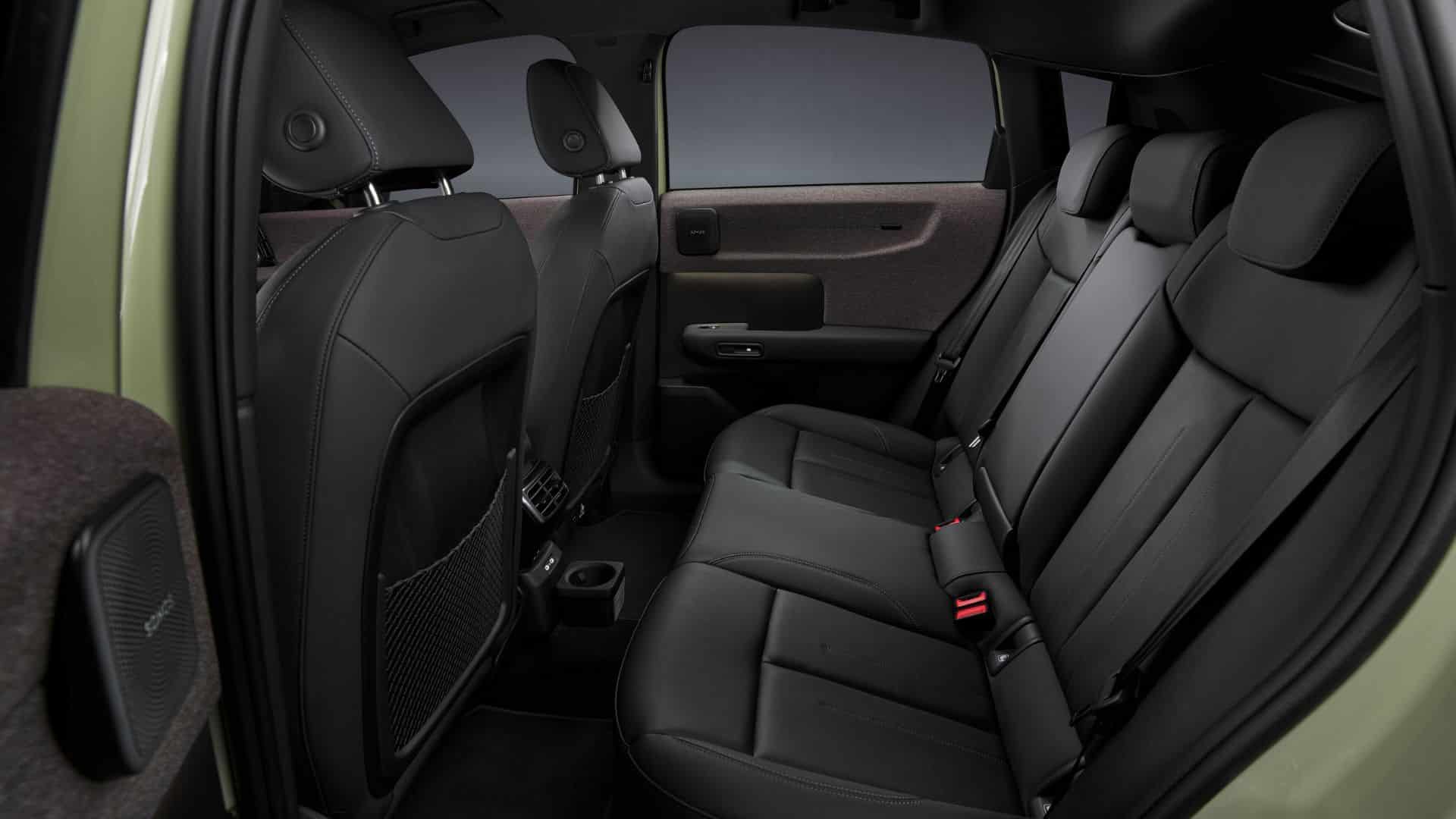 Vista do banco do passageiro dianteiro do Audi em couro preto com costuras claras, apoiado por um apoio de braço central elevado. Ao fundo, vê-se o painel da porta com acabamento em tecido