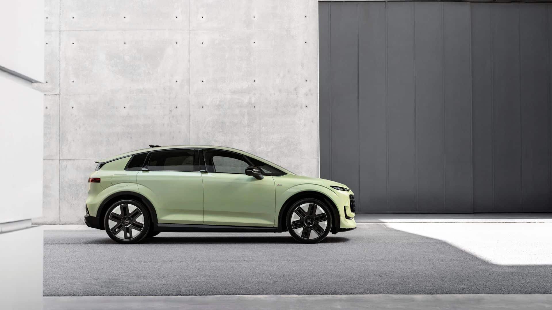 Perfil lateral do Audi na cor verde-claro, estacionado entre paredes de concreto bruto e uma porta metálica escura. A silhueta mostra as linhas suaves do SUV elétrico e os retrovisores sem haste