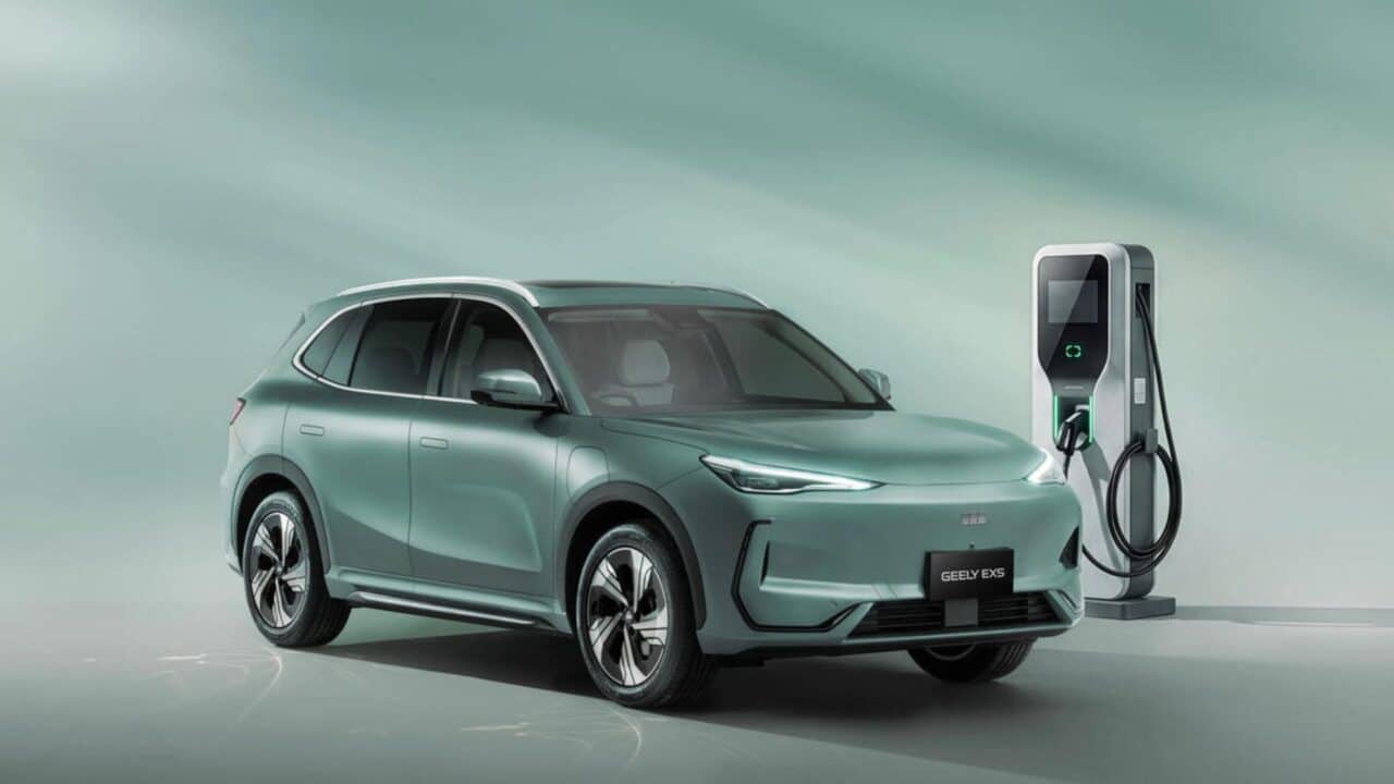 SUV elétrico da Geely verde-claro em um estúdio, estacionado ao lado de uma estação de carregamento elétrico