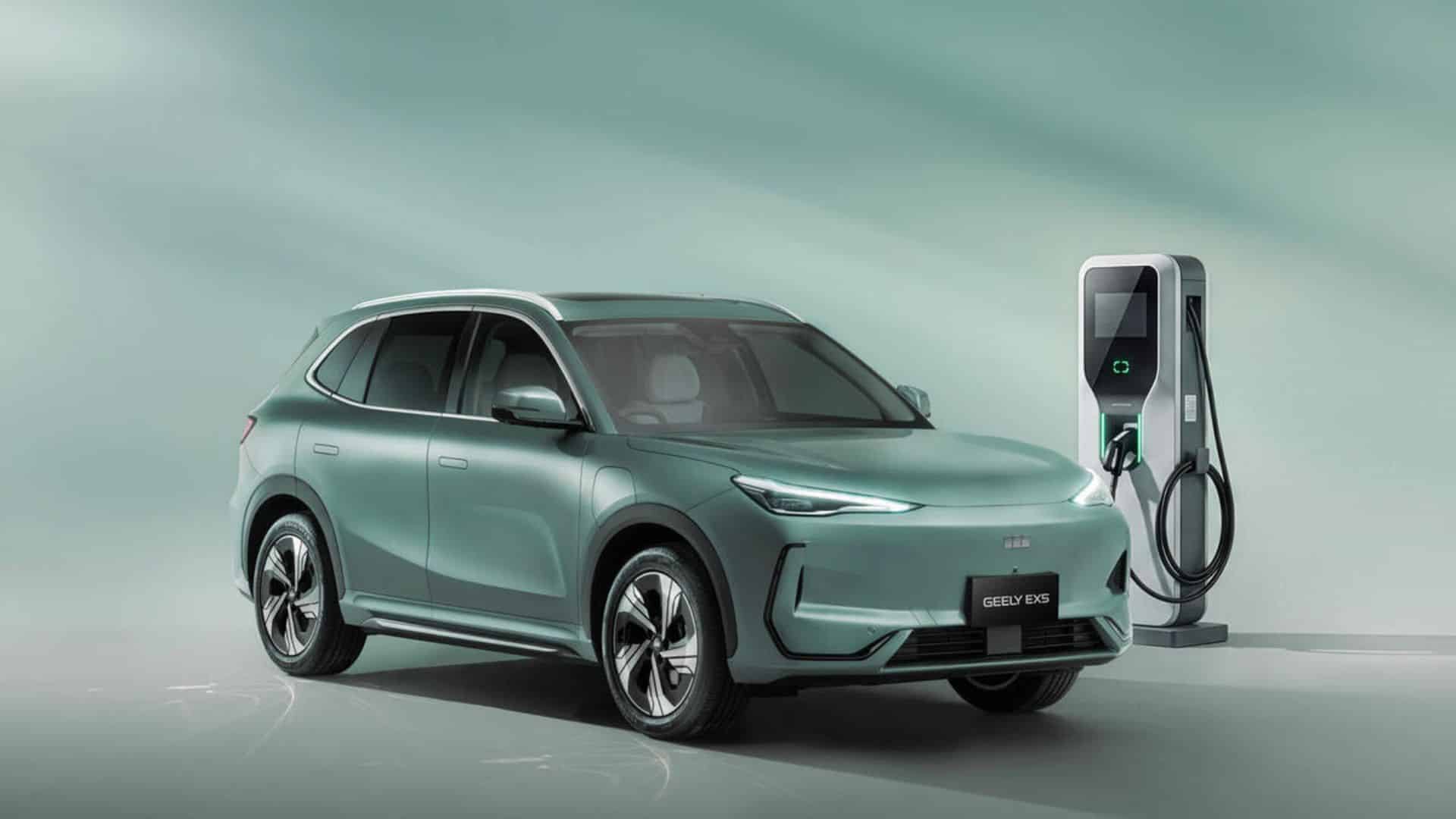 SUV elétrico da Geely verde-claro em um estúdio, estacionado ao lado de uma estação de carregamento elétrico