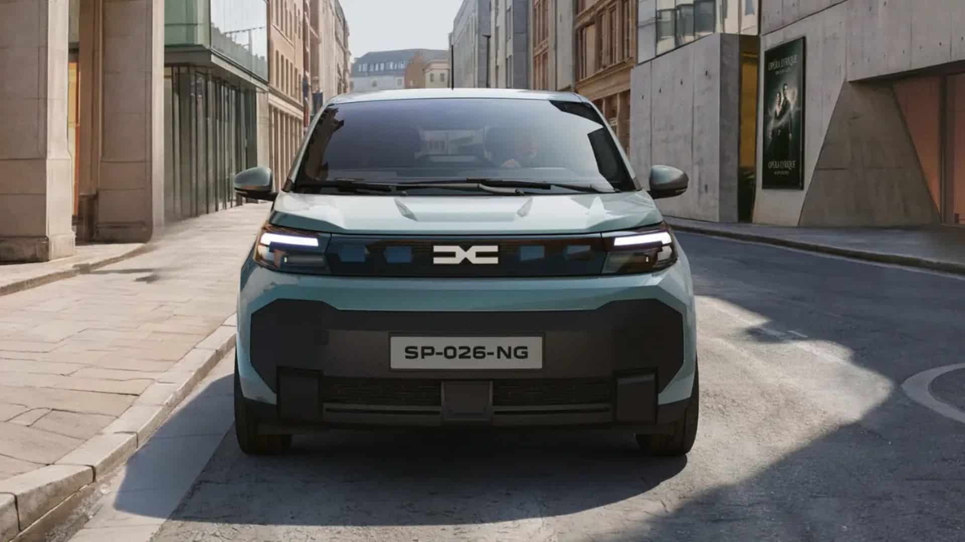 Vista frontal do Dacia Spring na cor verde-água. O carro possui faróis em LED em formato de 'C', uma barra preta central com o logo 'DC' e um grande para-choque inferior preto de design robusto