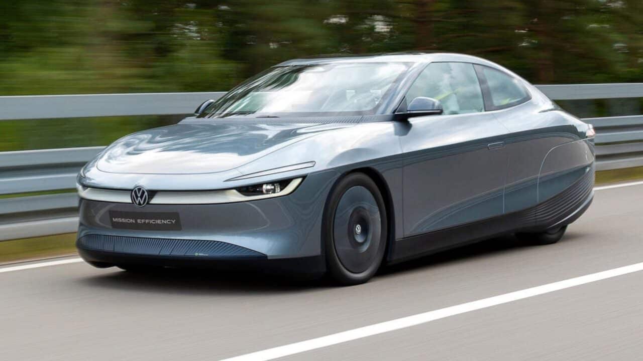 Carro-conceito Volkswagen Mission Efficiency em movimento, visto de frente. O veículo elétrico tem cor azul-acinzentada metálica, design aerodinâmico com faróis finos de LED e o logotipo da Volkswagen iluminado na grade frontal