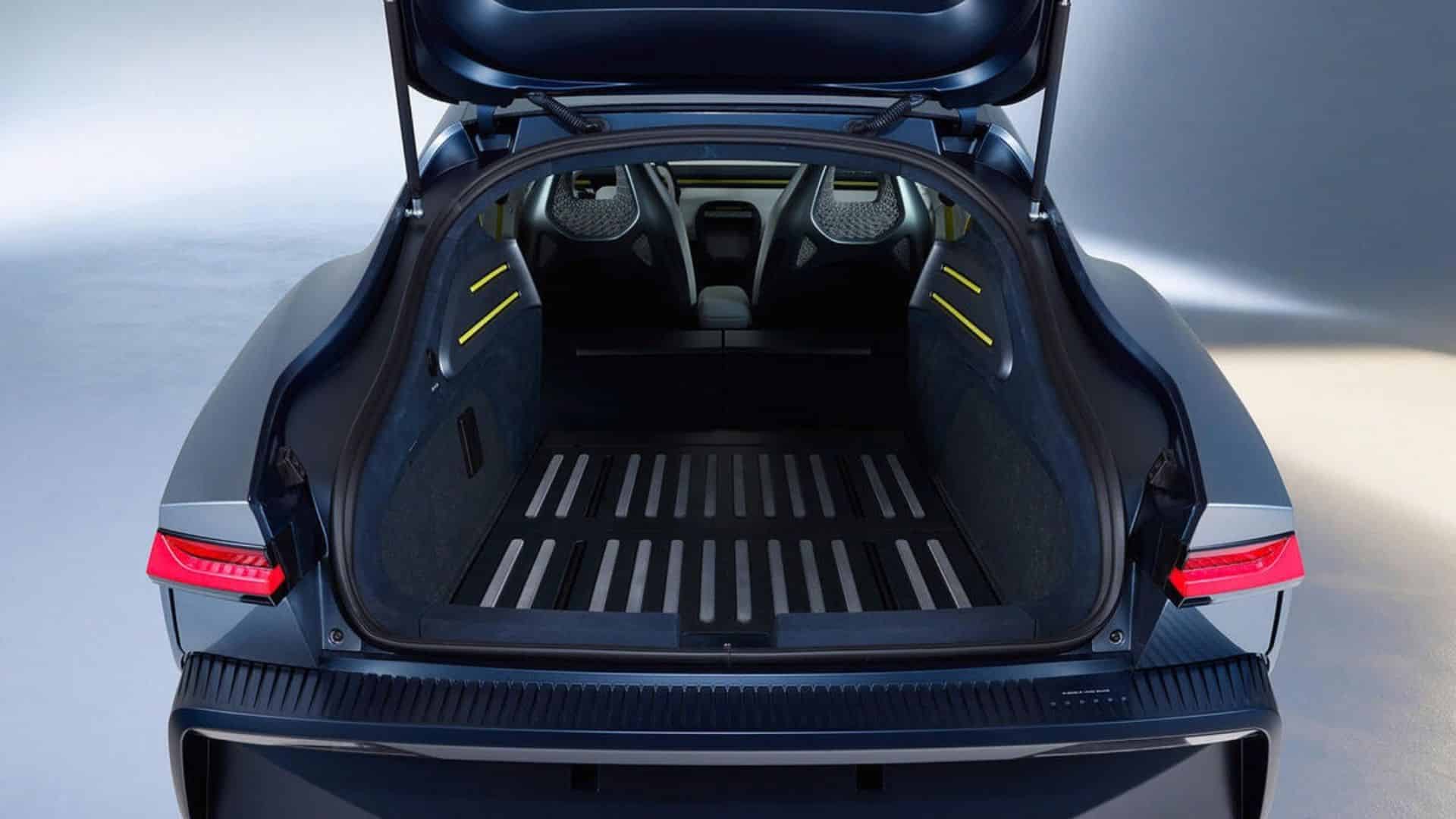 Porta-malas traseiro do Volkswagen Mission Efficiency aberto, revelando um compartimento de bagagem espaçoso com piso de alumínio canelado e detalhes em amarelo nas laterais. O interior do veículo e as lanternas traseiras acesas também são visívei