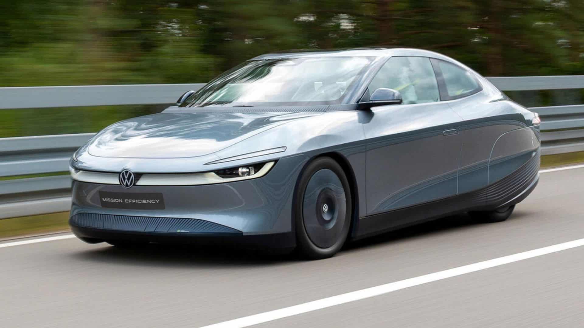 Carro-conceito Volkswagen Mission Efficiency em movimento, visto de frente. O veículo elétrico tem cor azul-acinzentada metálica, design aerodinâmico com faróis finos de LED e o logotipo da Volkswagen iluminado na grade frontal