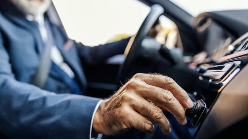 Imagem dentro de um carro mostrando um motorista idoso mexendo em um controle do carro