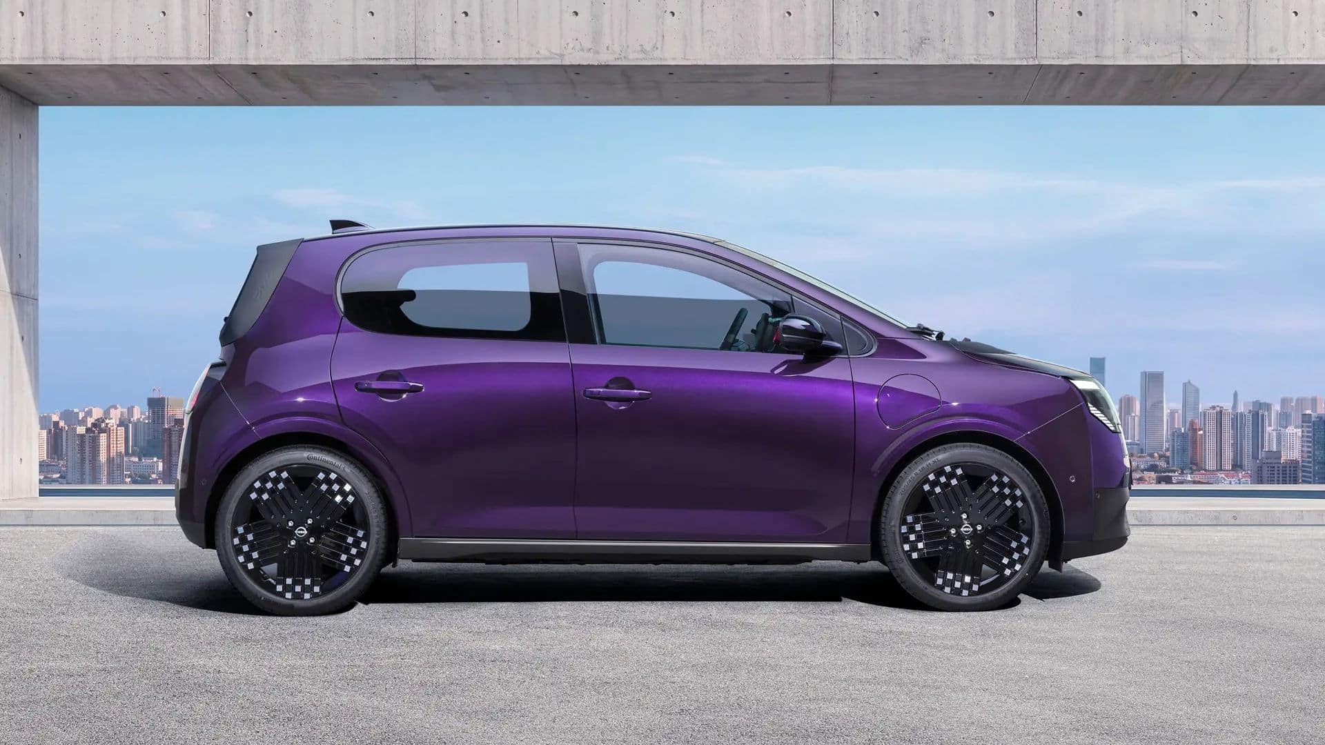 Vista lateral do Nissan PIXO na cor roxa metálica, estacionado sob uma estrutura de concreto. O carro tem formato compacto, rodas de liga leve com detalhes prateados e vidros escurecidos, com o horizonte de uma cidade ao fundo
