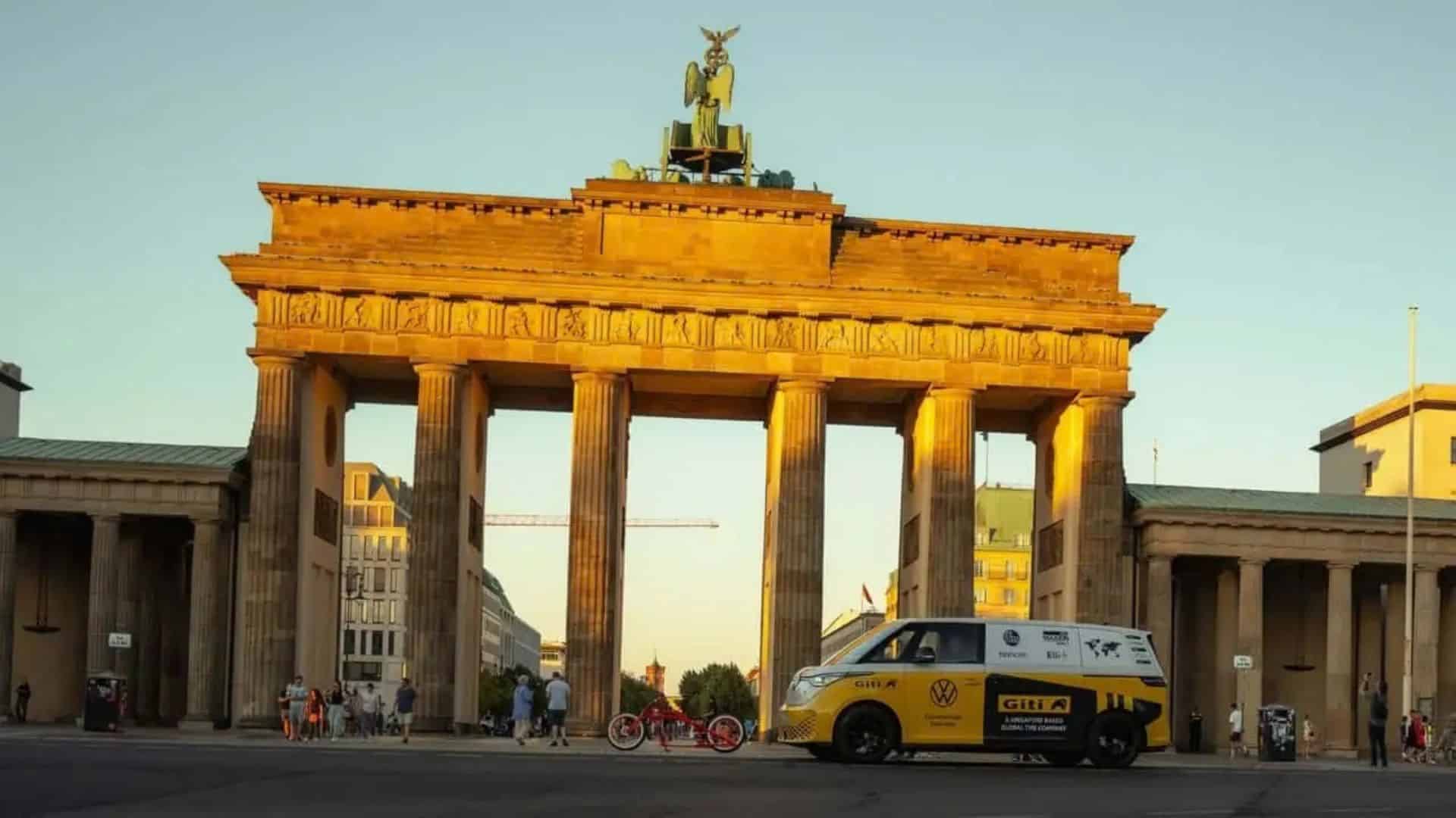 VW ID. Buzz na viagem recordista de Rainer Zietlow.  VW ID. Buzz amarelo e branco estacionado em frente ao Portão de Brandemburgo, em Berlim, iluminado pela luz dourada do pôr do sol