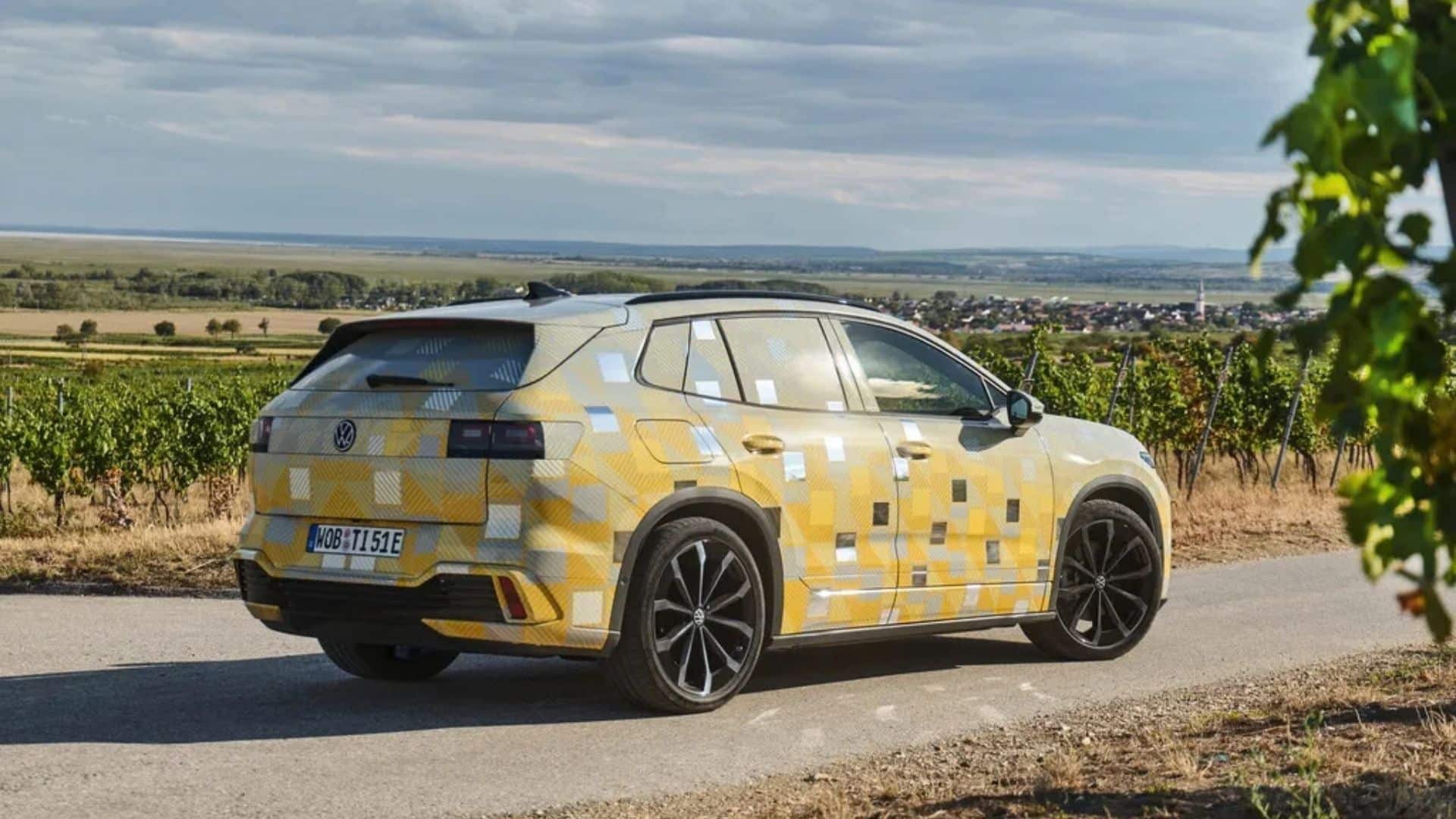 Protótipo camuflado do Volkswagen ID. Tiguan 2027 visto de traseira e lateral, em uma estrada com vinhedos ao fundo