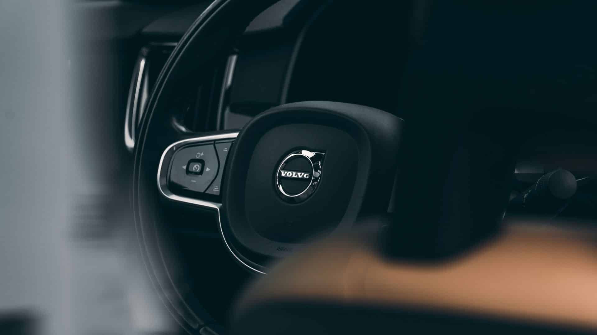 Volante de um carro Volvo visto em close-up, com acabamento em couro preto e o logotipo circular da Volvo em cromado ao centro