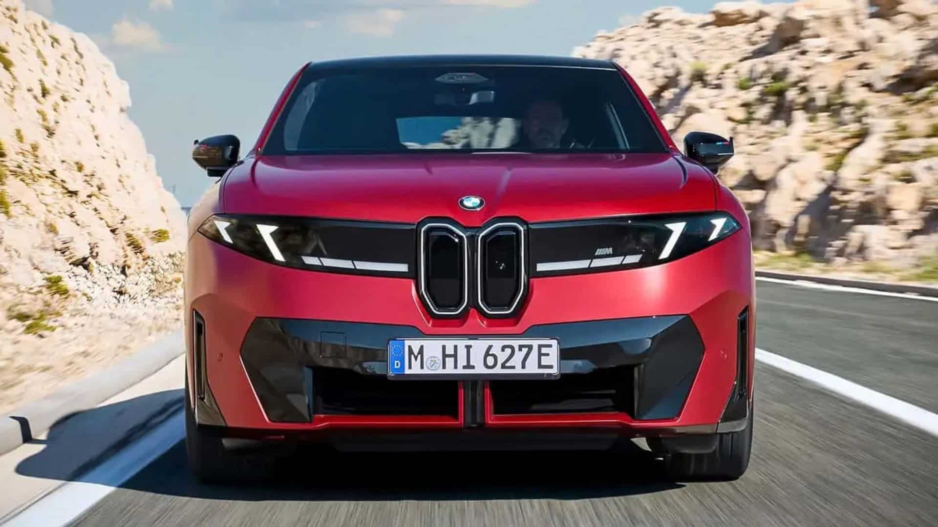 Vista frontal do BMW iX4 vermelho em movimento, mostrando a face da Neue Klasse com o duplo rim e os faróis fundidos em uma única unidade gráfica, além do para-choque dianteiro com elementos da linguagem de design BMW M