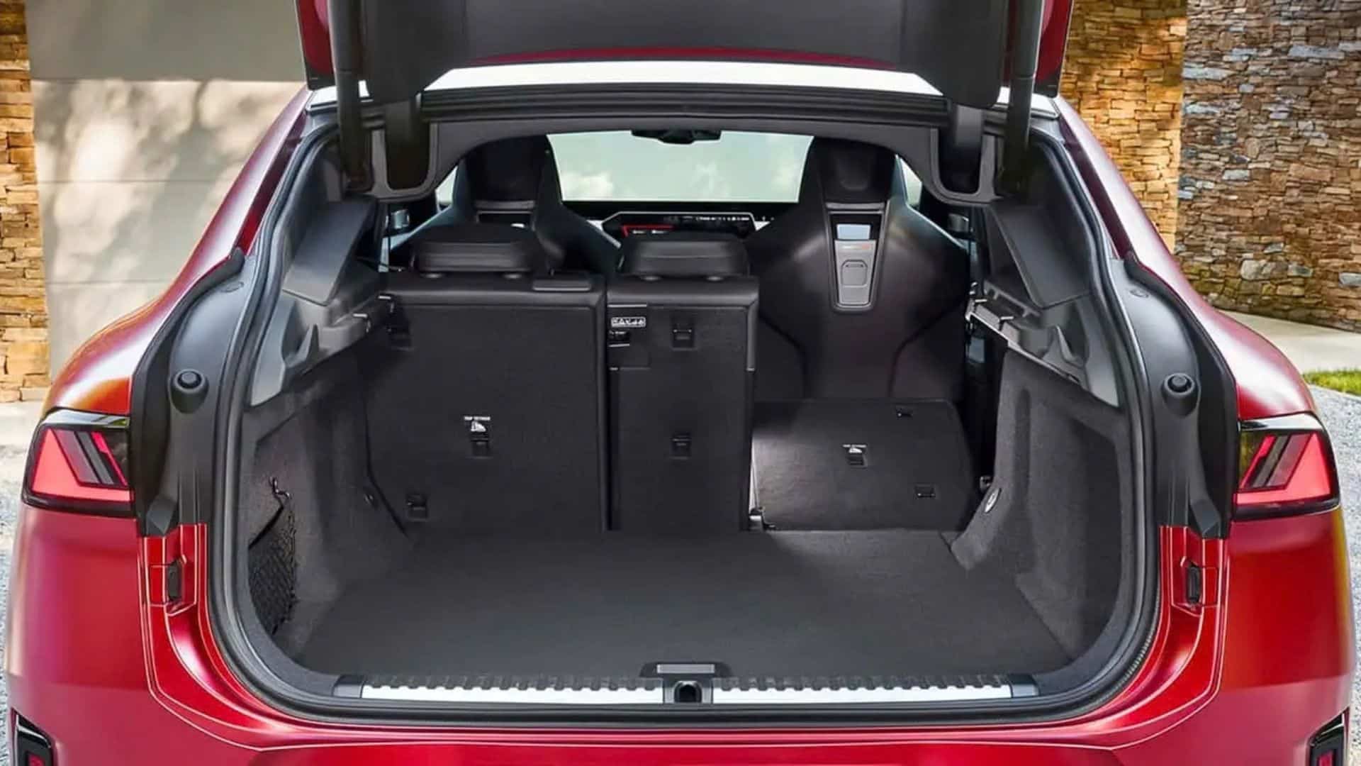 Vista do porta-malas aberto do BMW iX4, mostrando o espaço de carga com acabamento em carpete preto, assentos traseiros rebatíveis e detalhes de fixação, além da tampa do porta-malas elevada