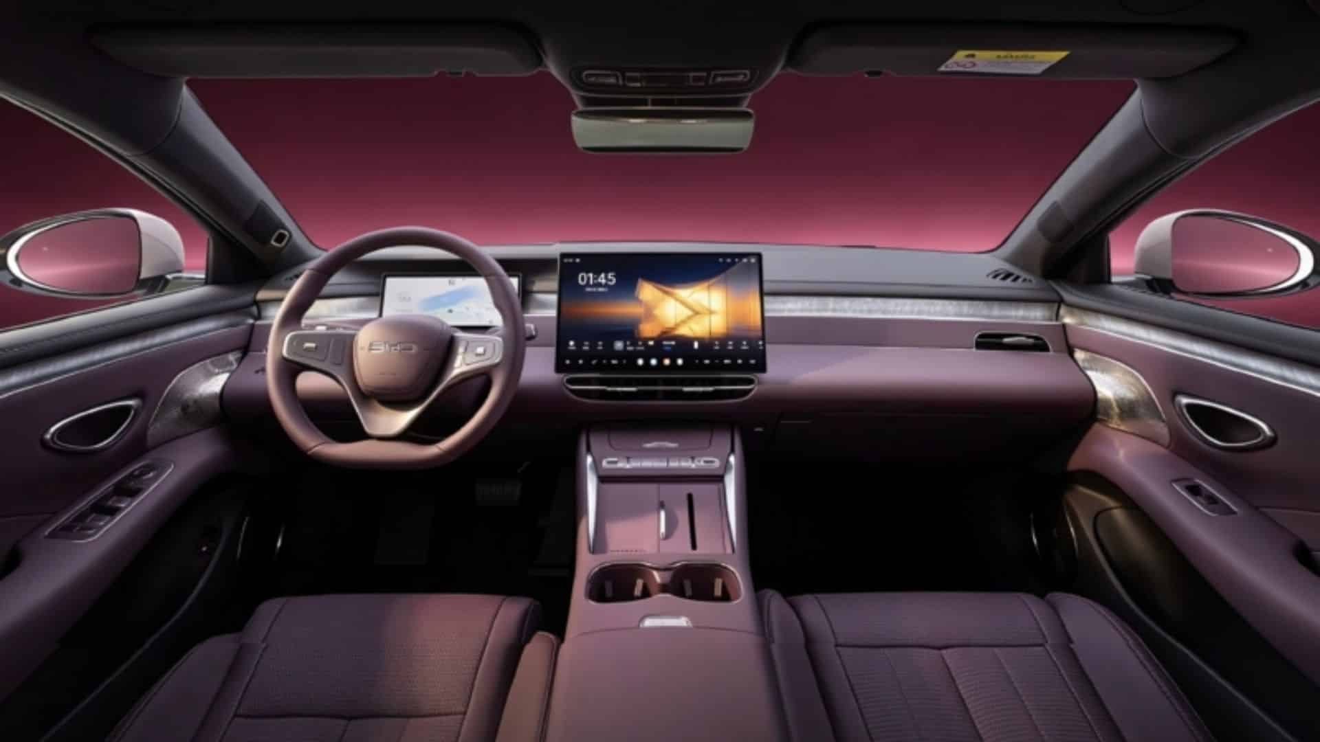 Interior do BYD Seal 07 com acabamento em tom de roxo escuro. A imagem mostra o painel de instrumentos digital, a grande tela central flutuante, o volante de três raios com o logotipo da BYD e o console central com dois porta-copos. Ao fundo, através do para-brisa, vê-se um céu em tons de rosa e roxo