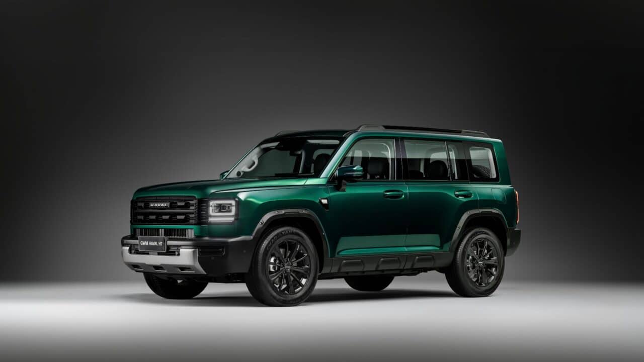 Vista lateral três quartos do GWM Haval H7, mostrando o design quadrado e robusto, teto com barras longitudinais, rodas de liga leve escurecidas, maçanetas convencionais e detalhes em preto nas caixas de roda e saias laterais